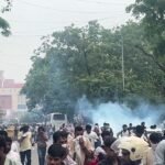 सड़क पर फैले धुएं के बीच पीछे हटते लोग और मौजूद पुलिसकर्मी